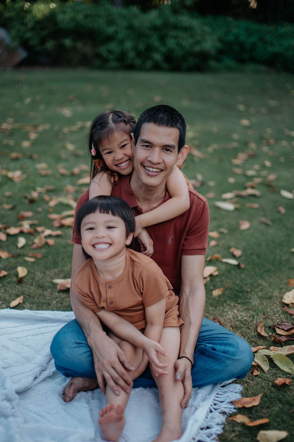 Three people sitting on blanket outdoors sharing joyful moment together during autumn photoshoot.