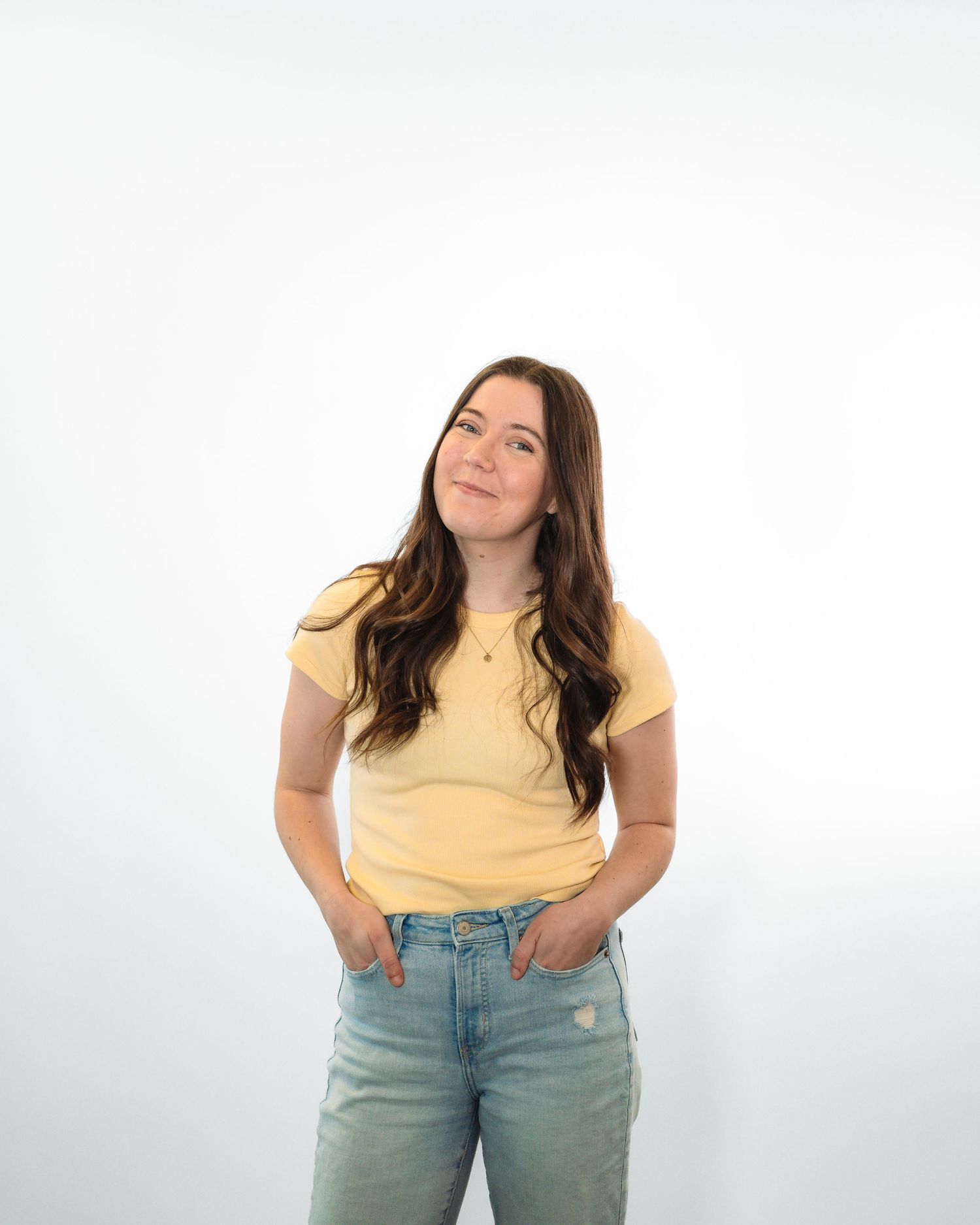 Person in yellow t-shirt and light jeans poses casually against white background.