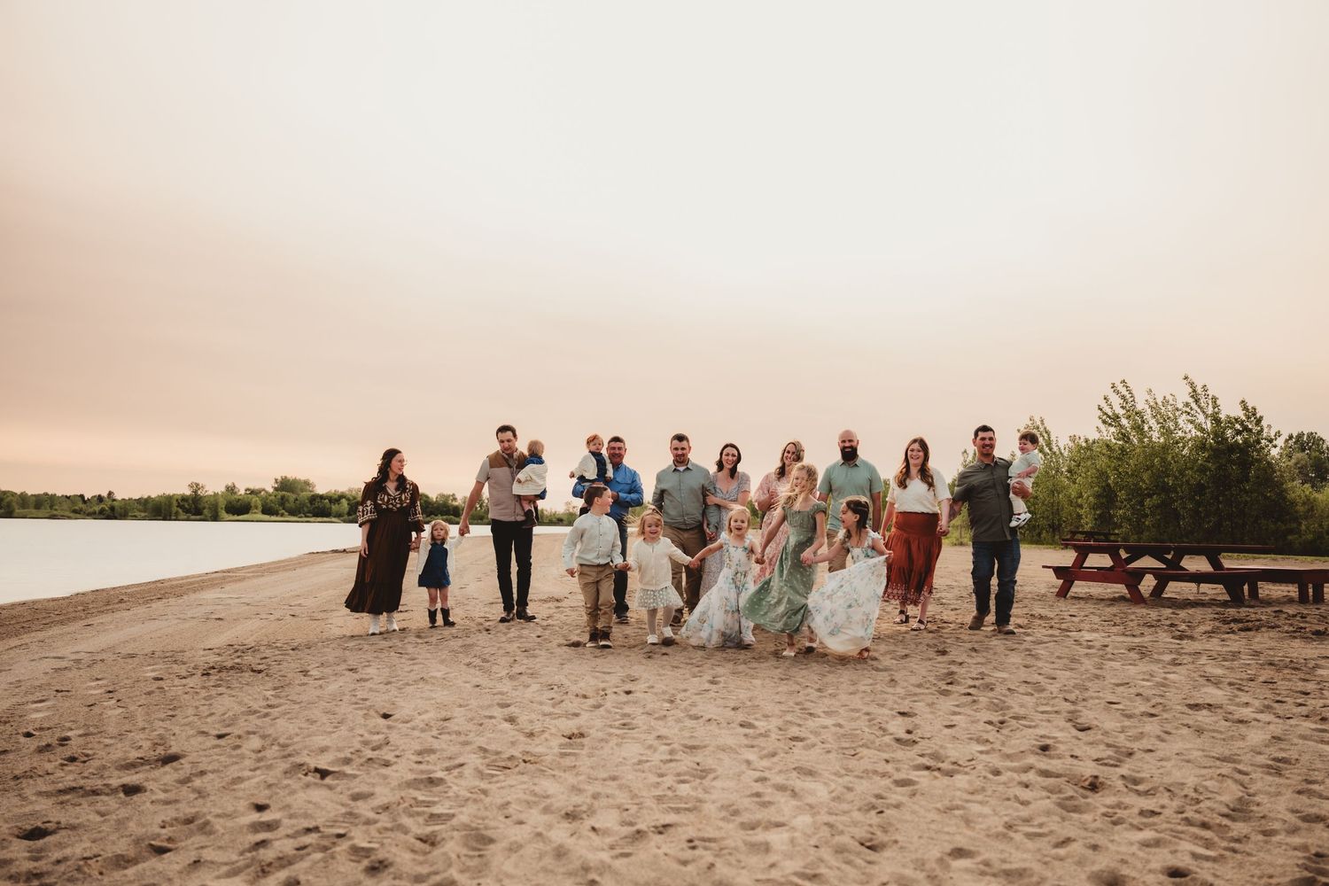 Wedding party walking in casual beachwear along a sandy beach shoreline at sunset.