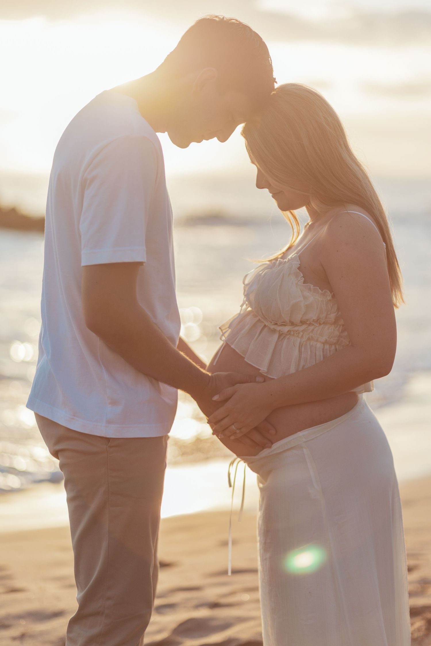 Expectant couple shares tender moment on beach at sunset as they embrace and celebrate pregnancy.