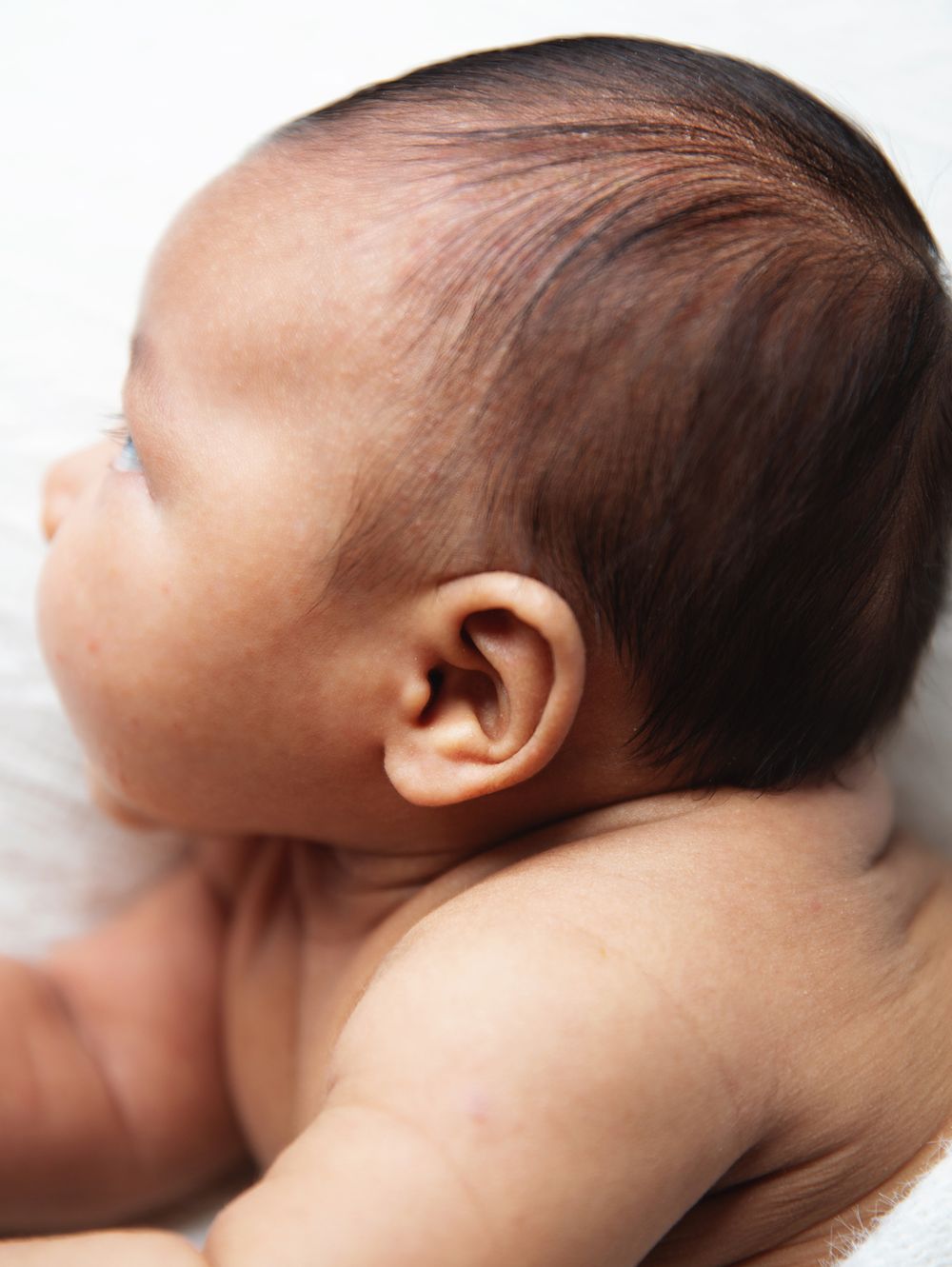 Close-up profile view of a baby's head with soft brown hair against a white background. During a newborn photoshoot in Sidcup