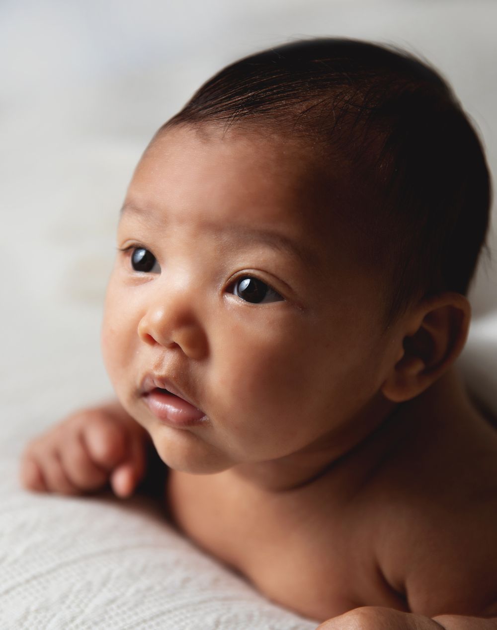 Close-up portrait of a baby lying on white fabric with soft lighting and warm tones. During a newborn photoshoot in London