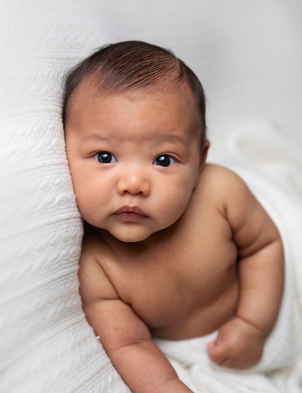 Close up portrait of a baby laying on white fabric wearing a diaper. During a newborn photoshoot in Bexley