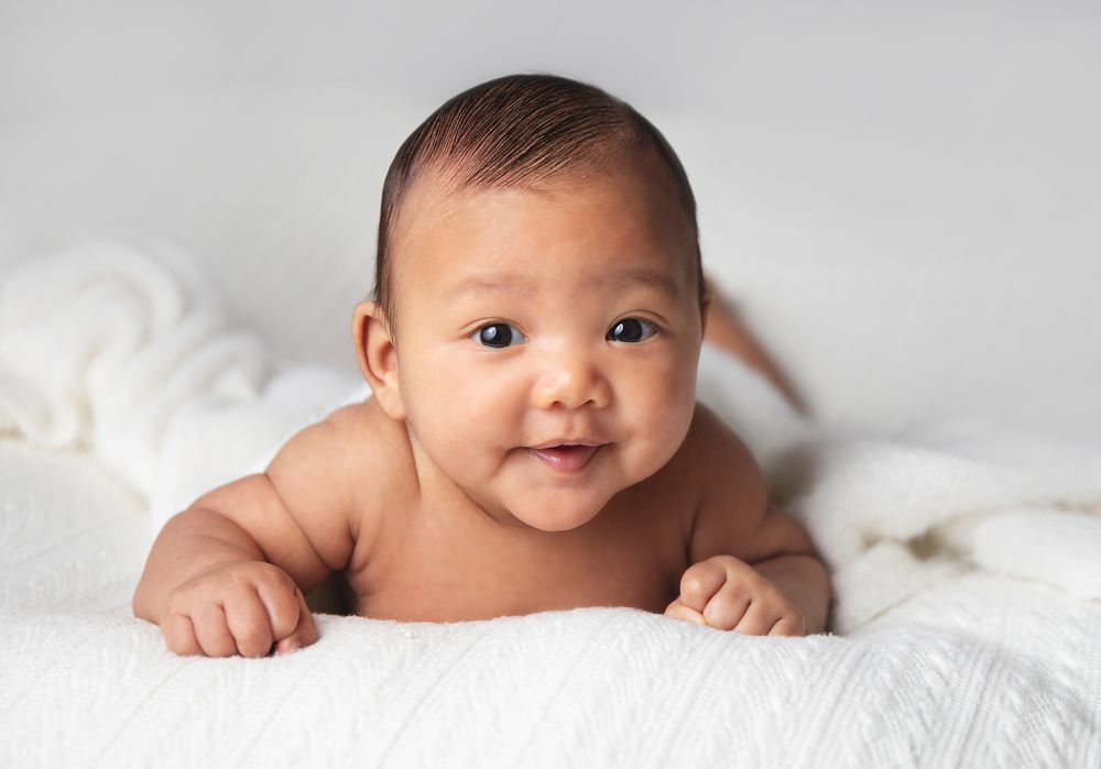 Baby lying on soft white blanket smiling and looking up at camera during newborn photography session. During a newborn photoshoot in London