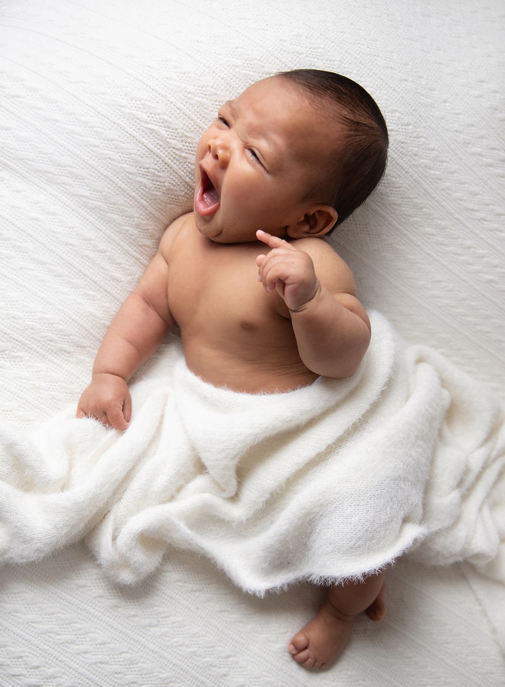 Laughing infant lying on white blanket during professional newborn photoshoot. During a newborn photoshoot in London