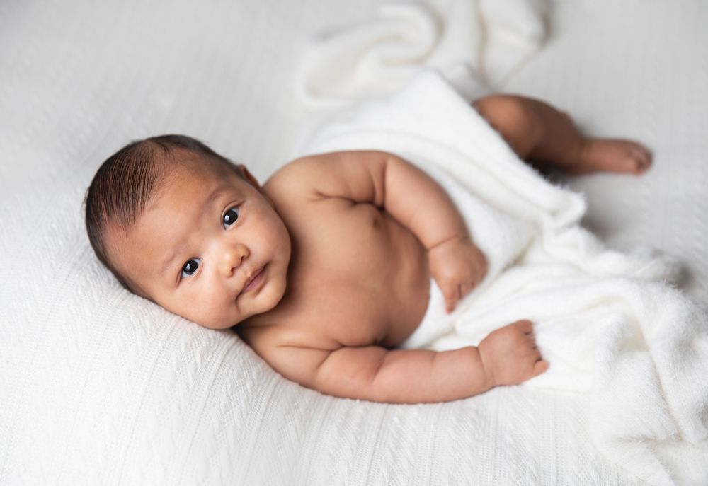Adorable newborn baby lying on white blanket during professional photo session with bright studio lighting. During a newborn session