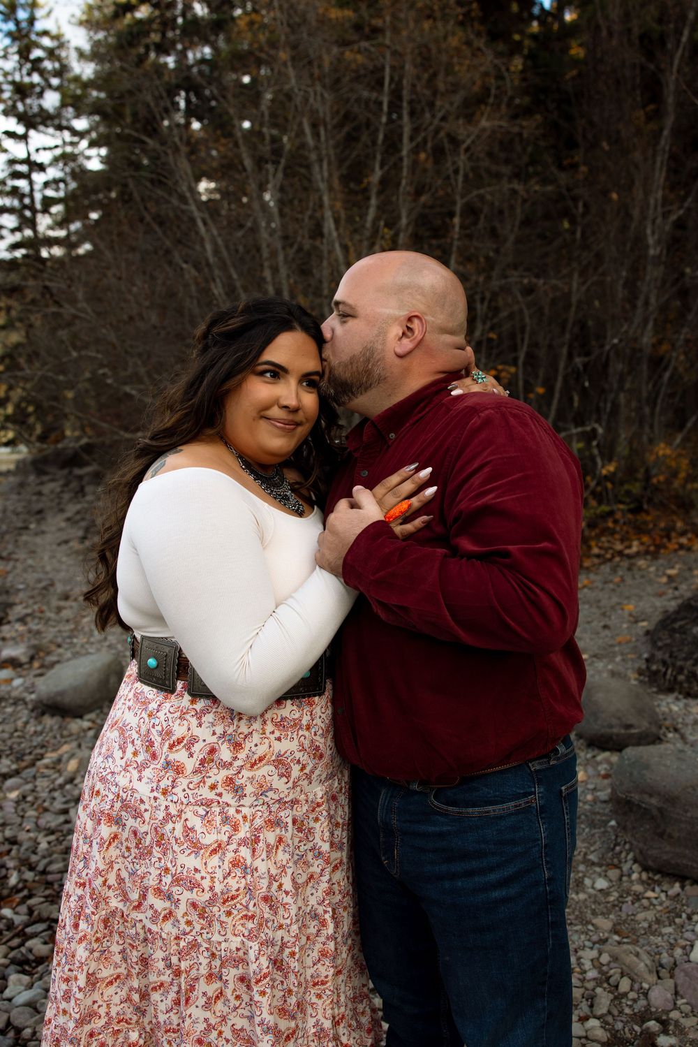 A romantic outdoor couple's photo with one person in a white sweater and floral skirt embracing their partner in burgundy.