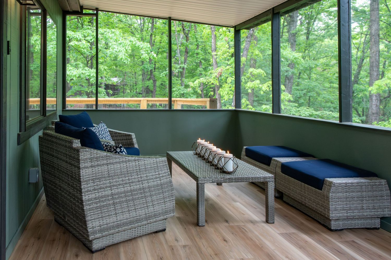 Modern screened porch with contemporary gray outdoor seating overlooks lush green forest views.