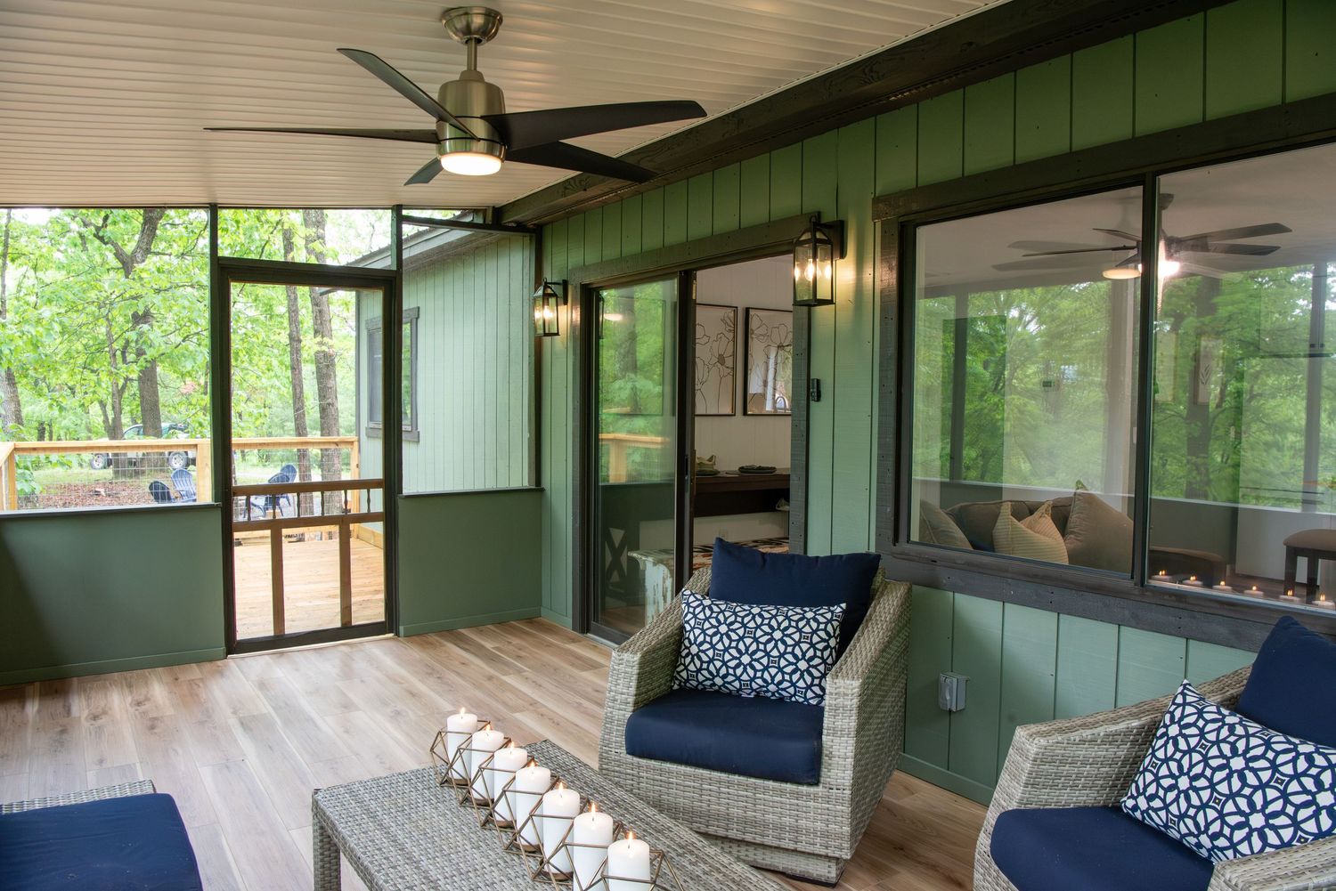 Sunlit screened porch with comfortable seating and green exterior walls.