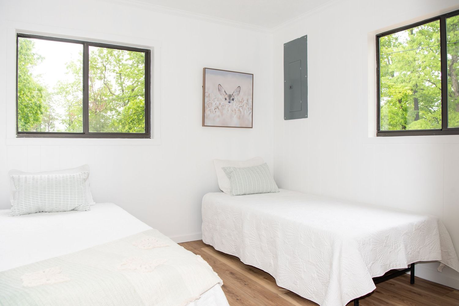 Minimalist bedroom with white bedding, natural light, and window views of trees.
