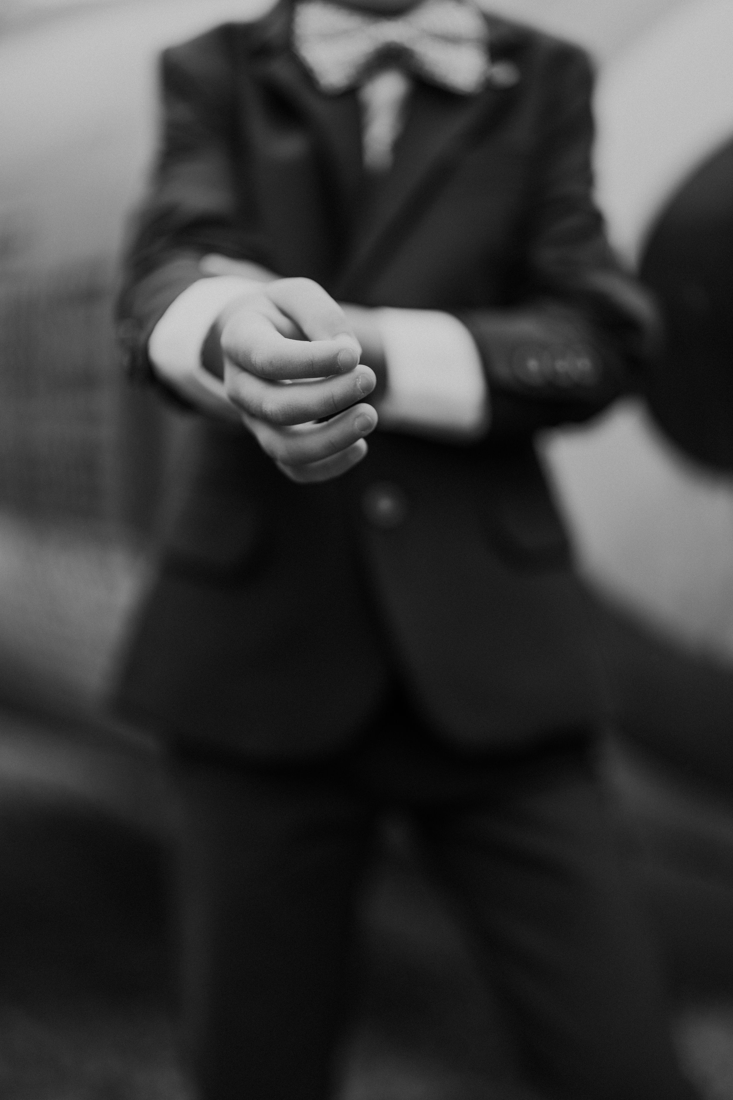 Zwart-wit close-up van handen friemelen met een ring, het dragen van formele kleding met een strik en pak.