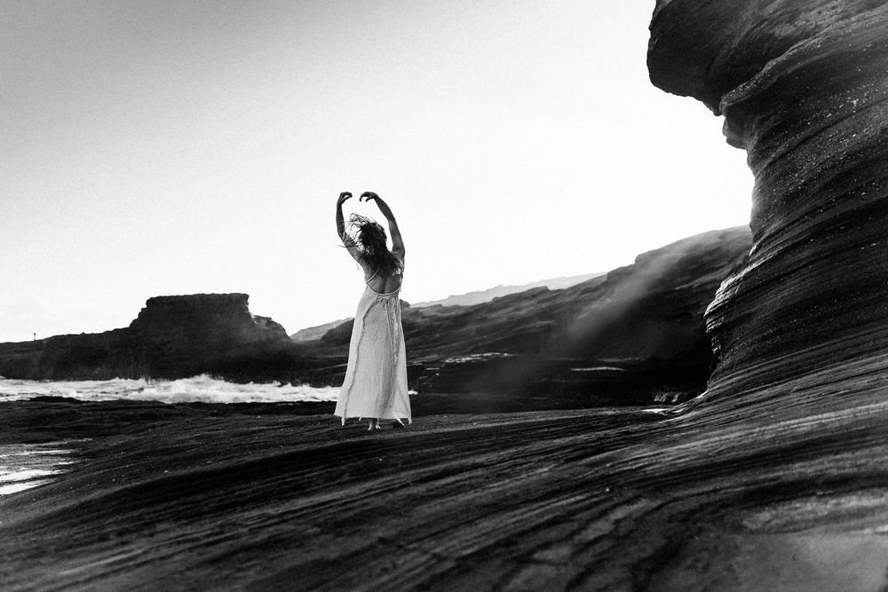 Ethereal figure in white dress walking along dramatic coastal cliffs at sunset.