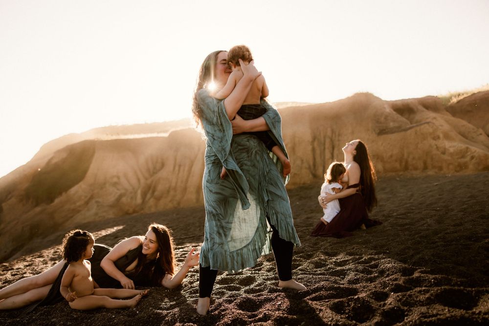 Women breastfeeding and playing with their toddlers enjoying sunset on desert mountain with dramatic lighting.