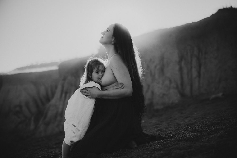 Tender breastfeeding embrace captured in black and white against mountain backdrop.