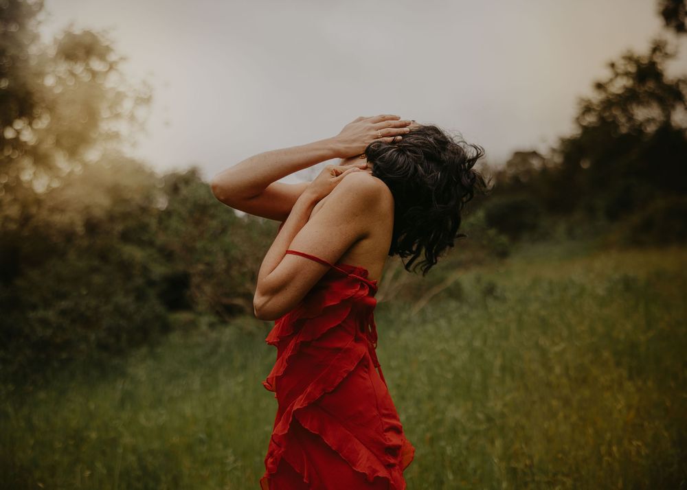 Person in flowing red dress dances in sunlit meadow.