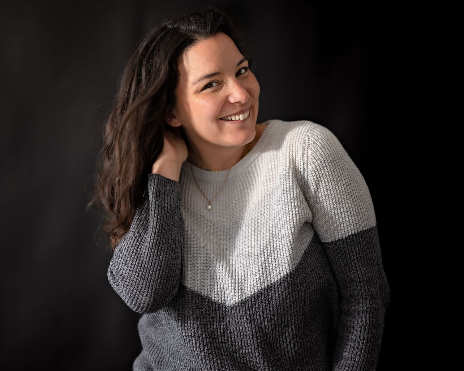 Portrait of someone wearing a comfortable gray and white color block sweater with jeans against a dark background.