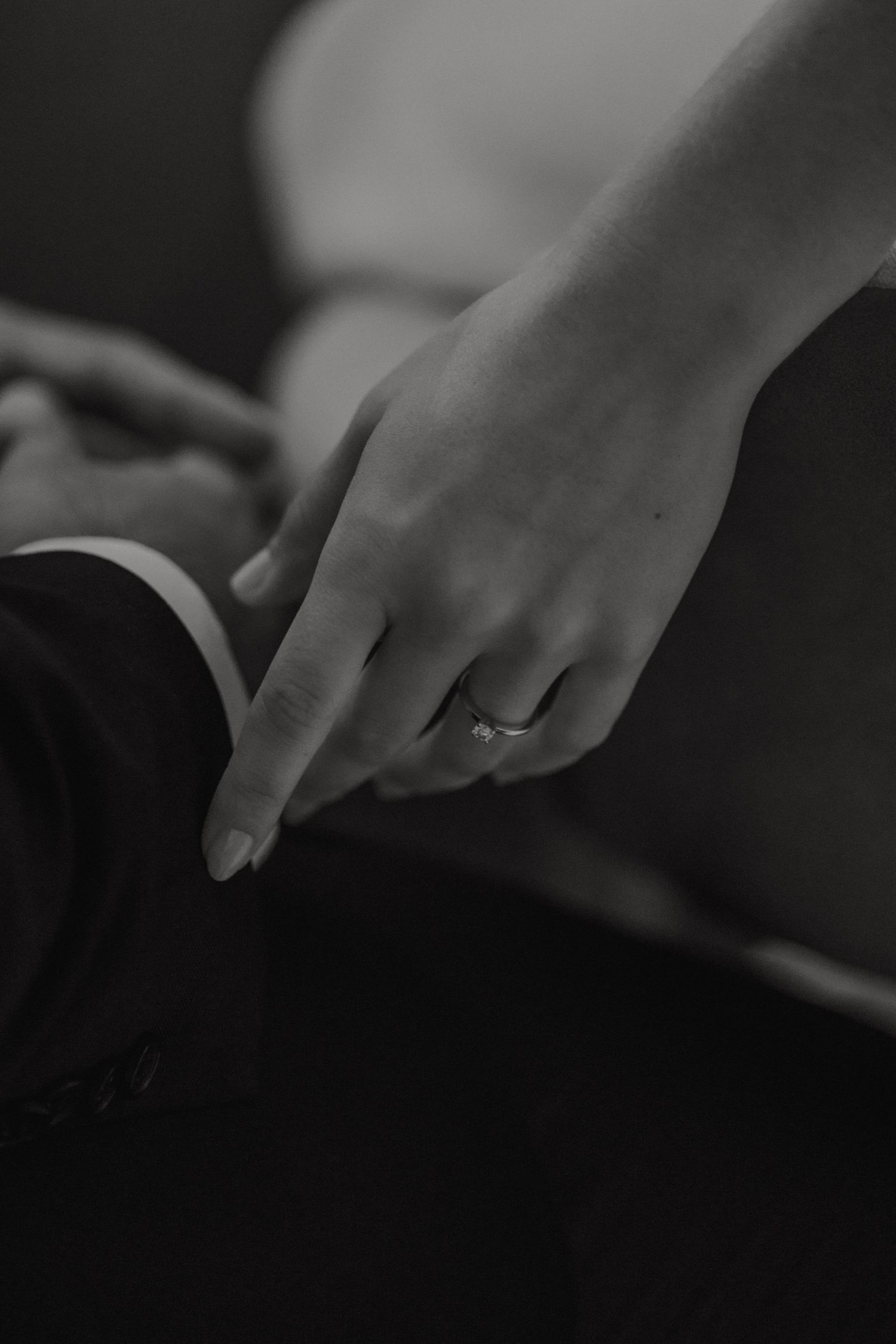 Close-up black and white photograph of a hand wearing an engagement ring.