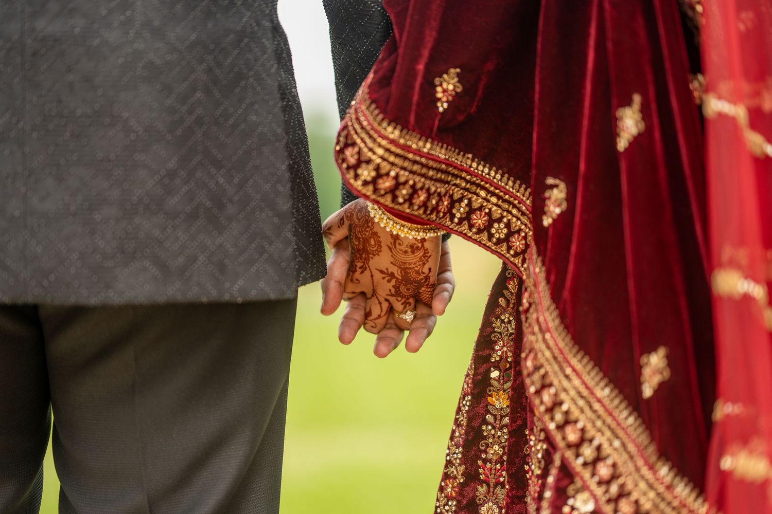 Indian bride in red sari with henna hands holding groom's hand at traditional wedding ceremony.