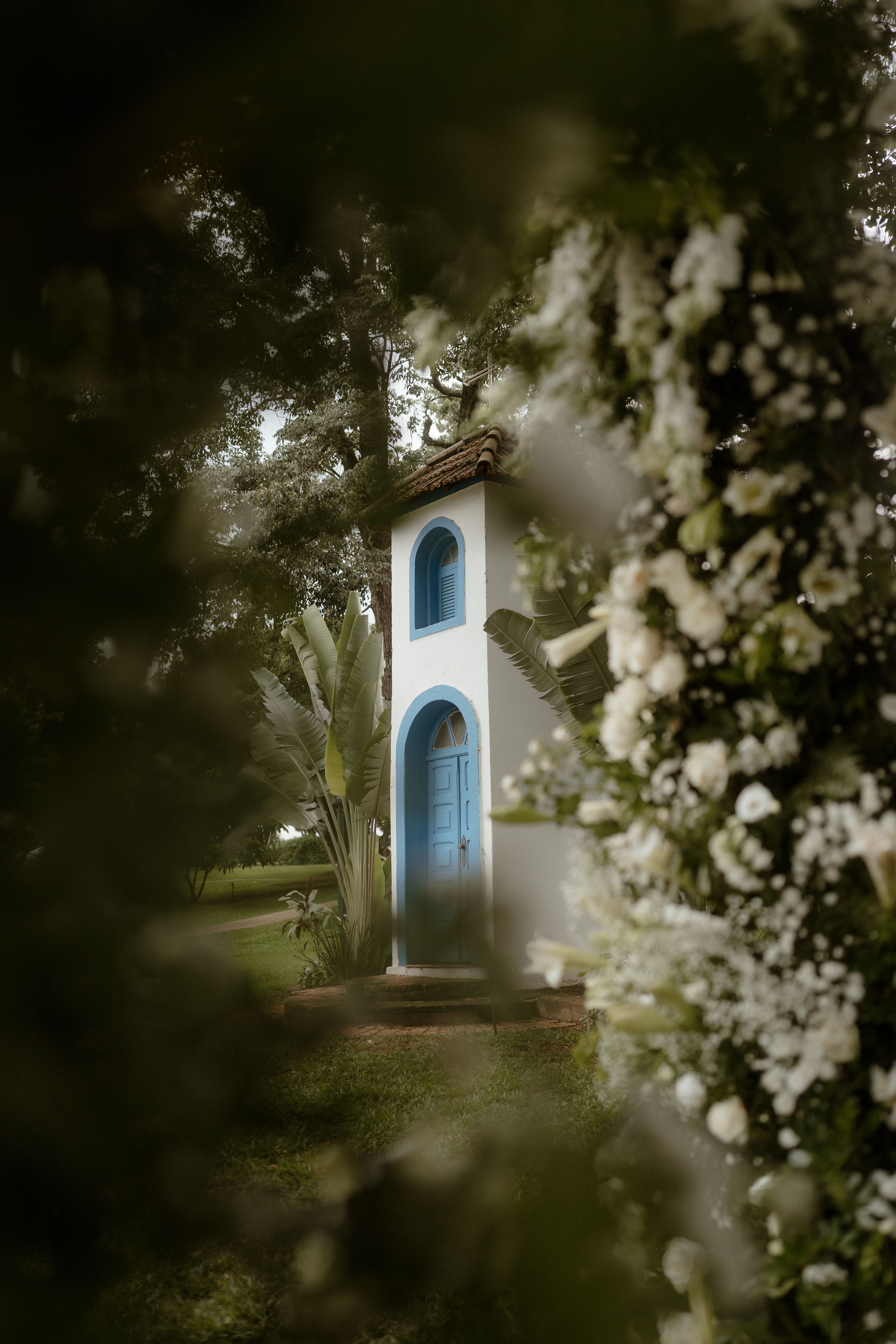 White chapel with blue doors framed by blooming flowers and foliage.