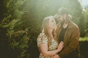A romantic couple embraces in a sunlit garden setting with golden light streaming through green foliage.