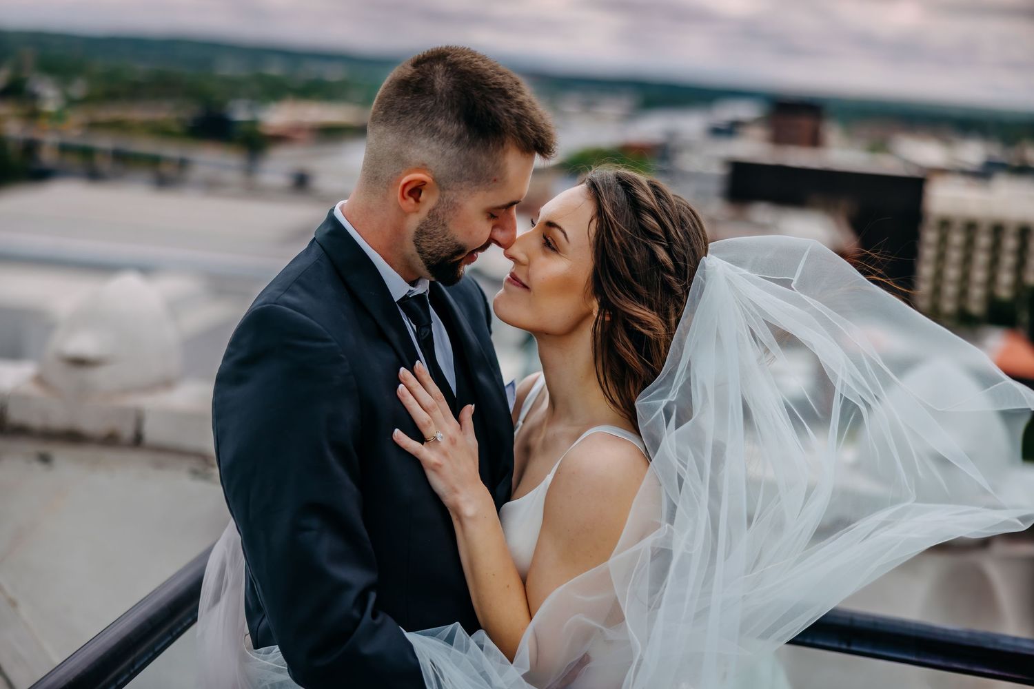 A bride and groom share an intimate moment on a rooftop with her flowing veil catching the breeze overlooking Grand Rapids Michigan