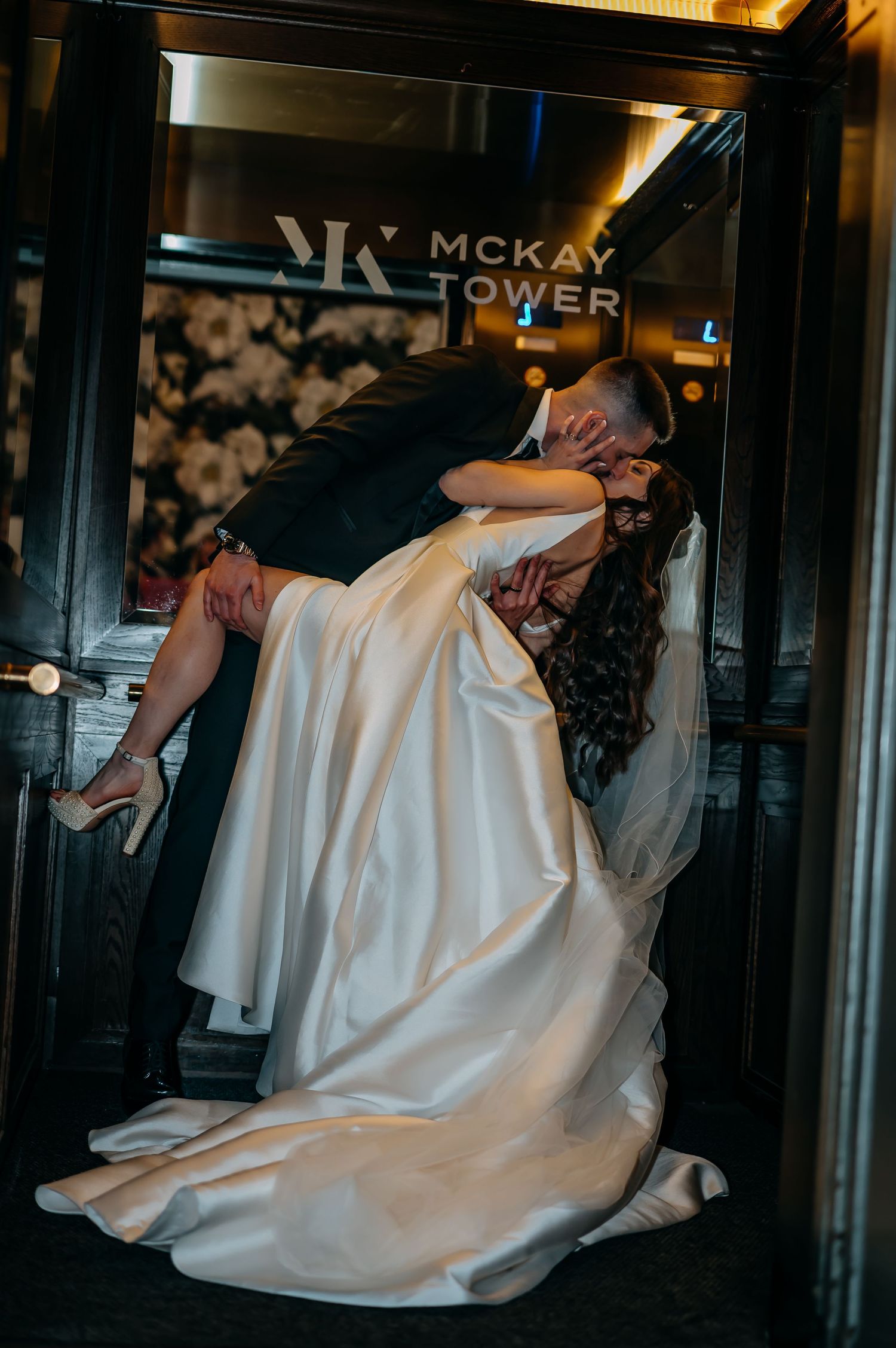 Romantic wedding couple embracing in front of illuminated Ballroom at McKay Tower building sign at night.