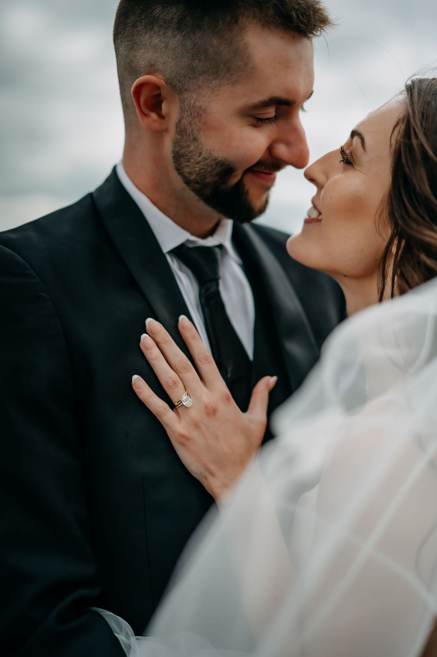 Close up portrait of a bride and groom sharing an intimate moment while showcasing her engagement ring in a moody setting.