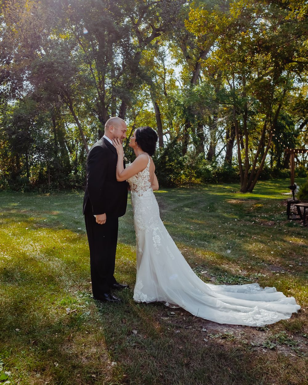 A romantic wedding portrait of a couple in a sunlit forest setting with a beautiful lace train dress.
