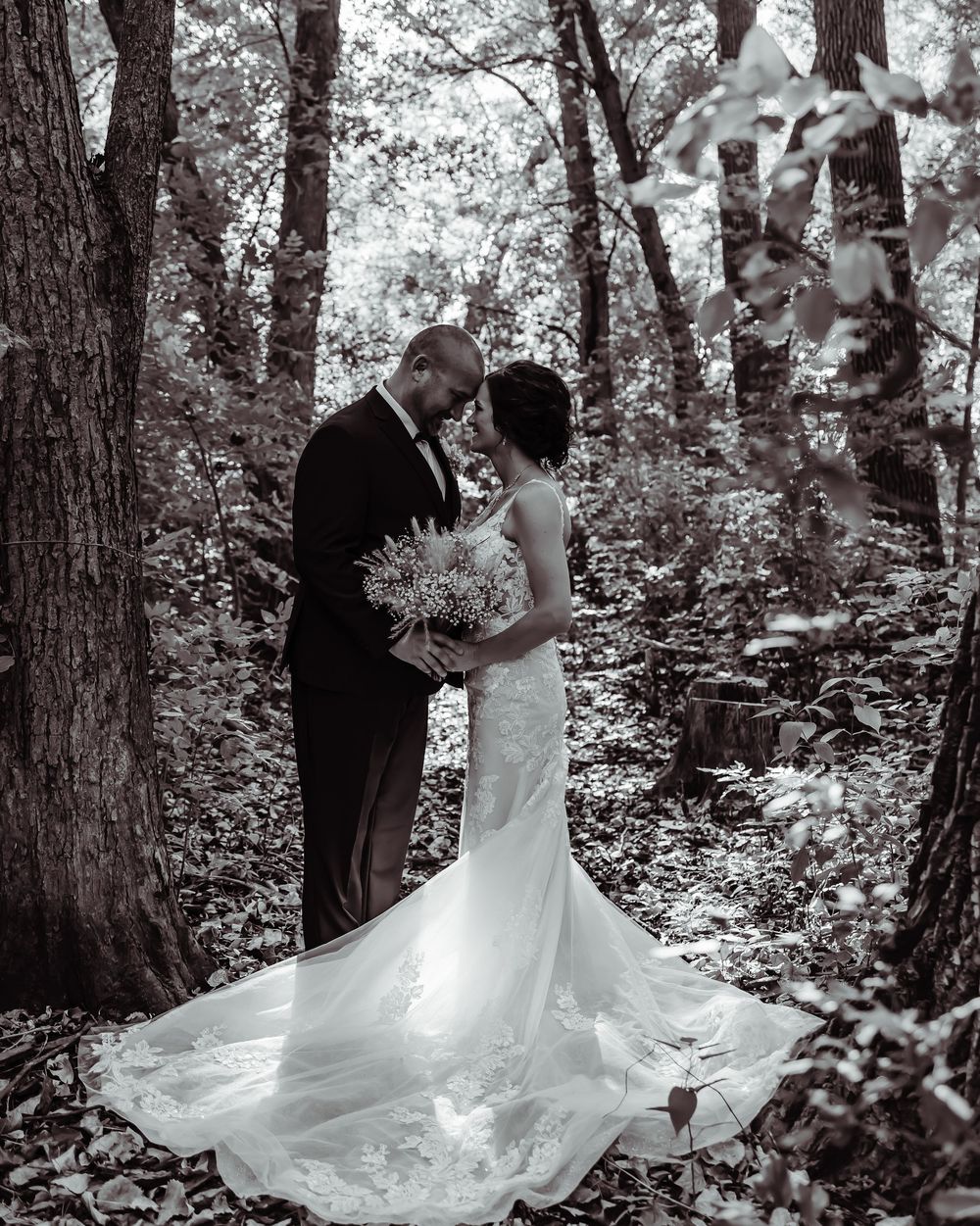 A romantic wedding photo of a couple in formal attire embracing in a misty forest setting.