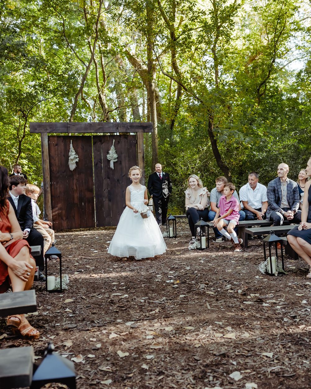 An intimate outdoor wedding ceremony in a rustic woodland setting with guests seated on benches.