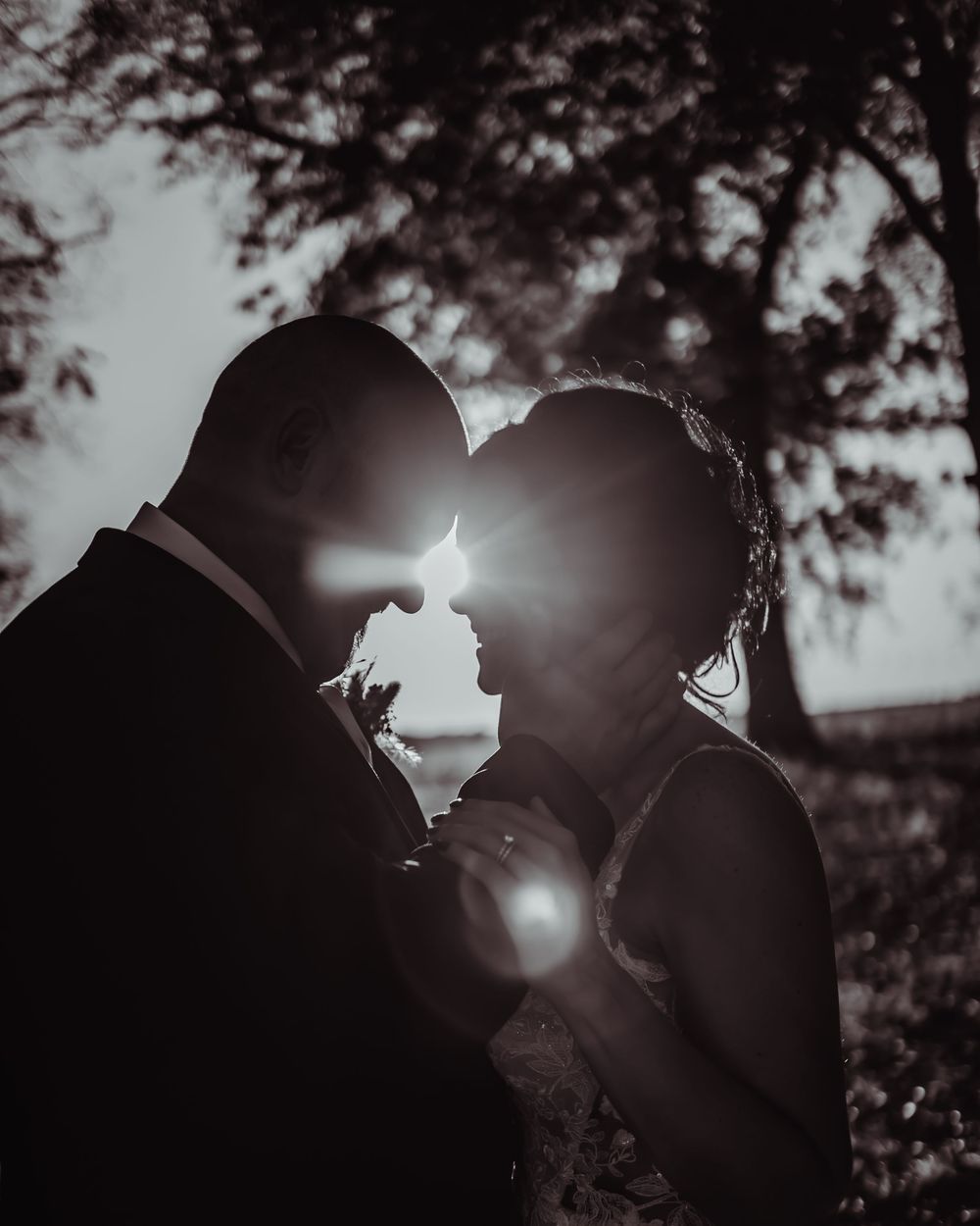 Silhouetted couple shares an intimate moment against dramatic sunset lighting in black and white.