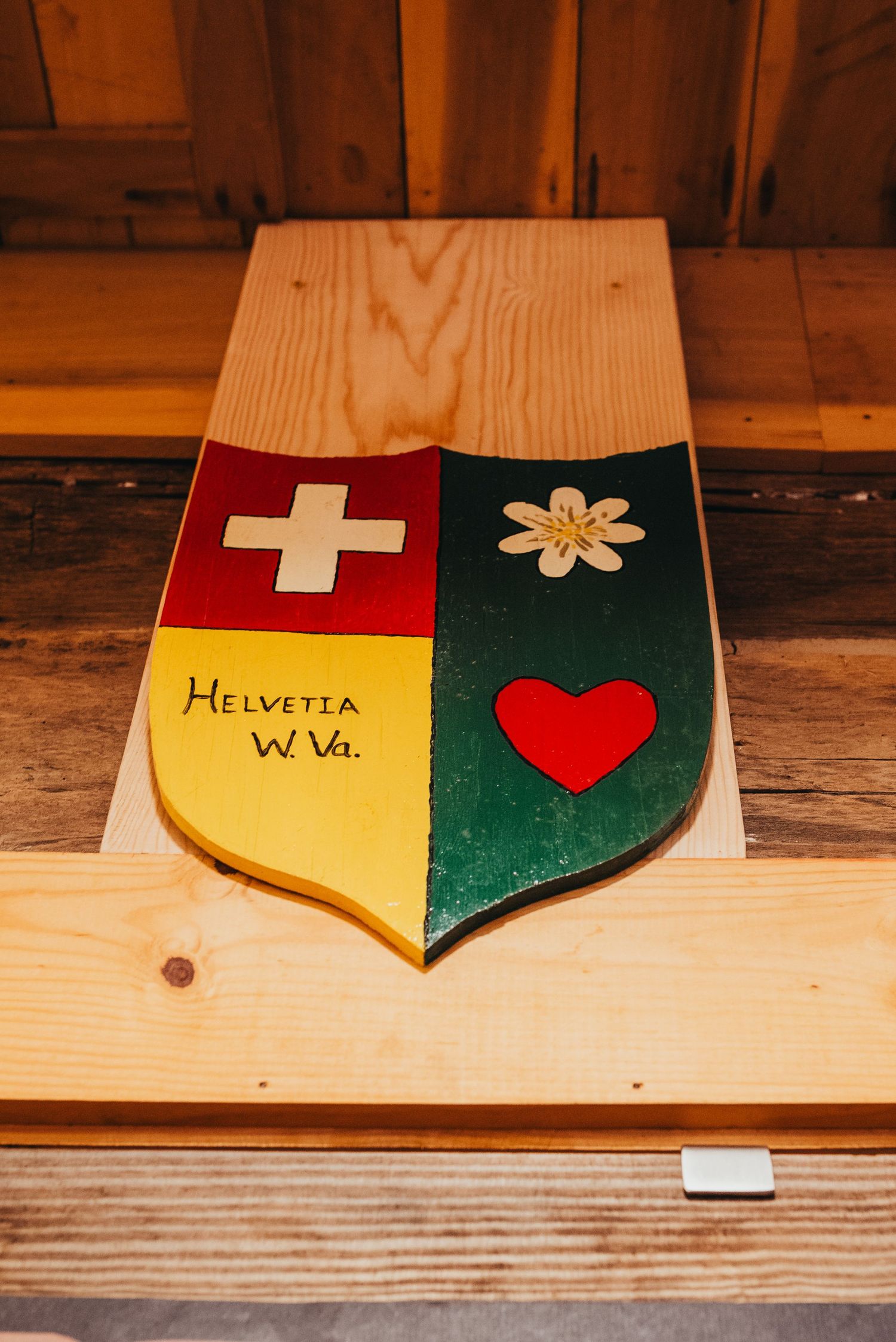Decorative wooden shield displaying Swiss cross and floral design with text 'Helvetia WV'.