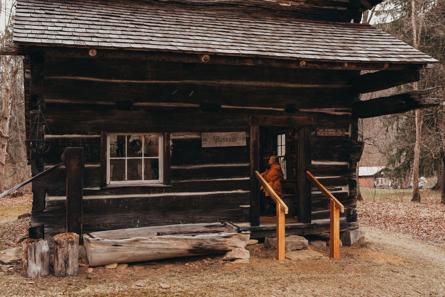 Historic log cabin with wooden porch and window in winter forest setting.