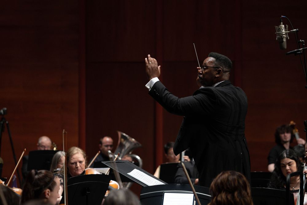 Conductor leading a full orchestra in a live classical music performance in a concert hall.