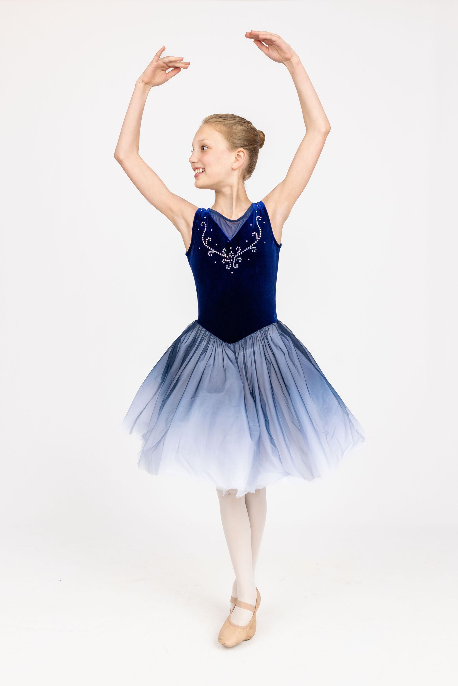Young ballet dancer in blue tutu dress performs graceful poses against white background.
