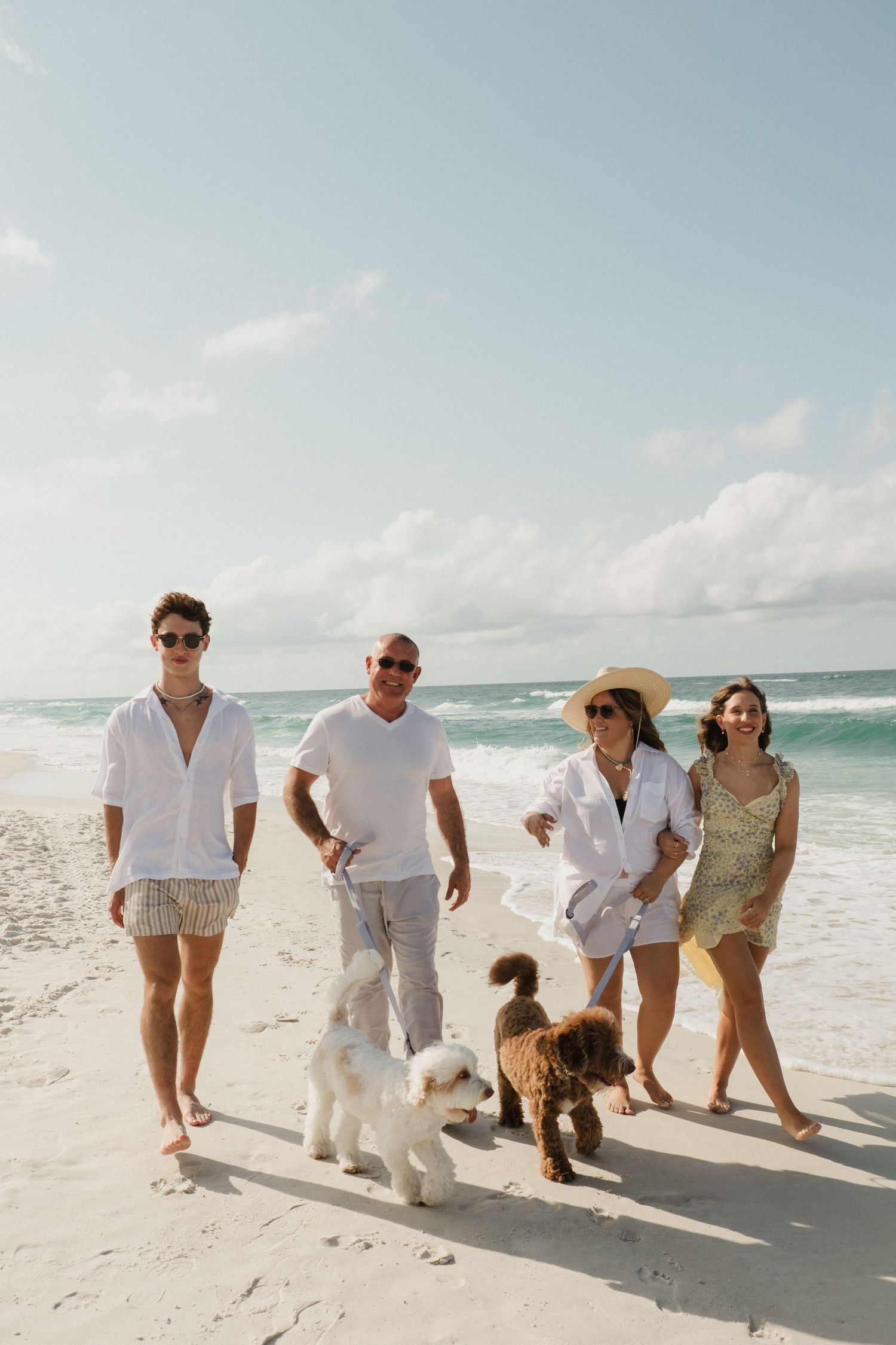 Group walking together along white sandy beach wearing coordinated white and beige outfits.