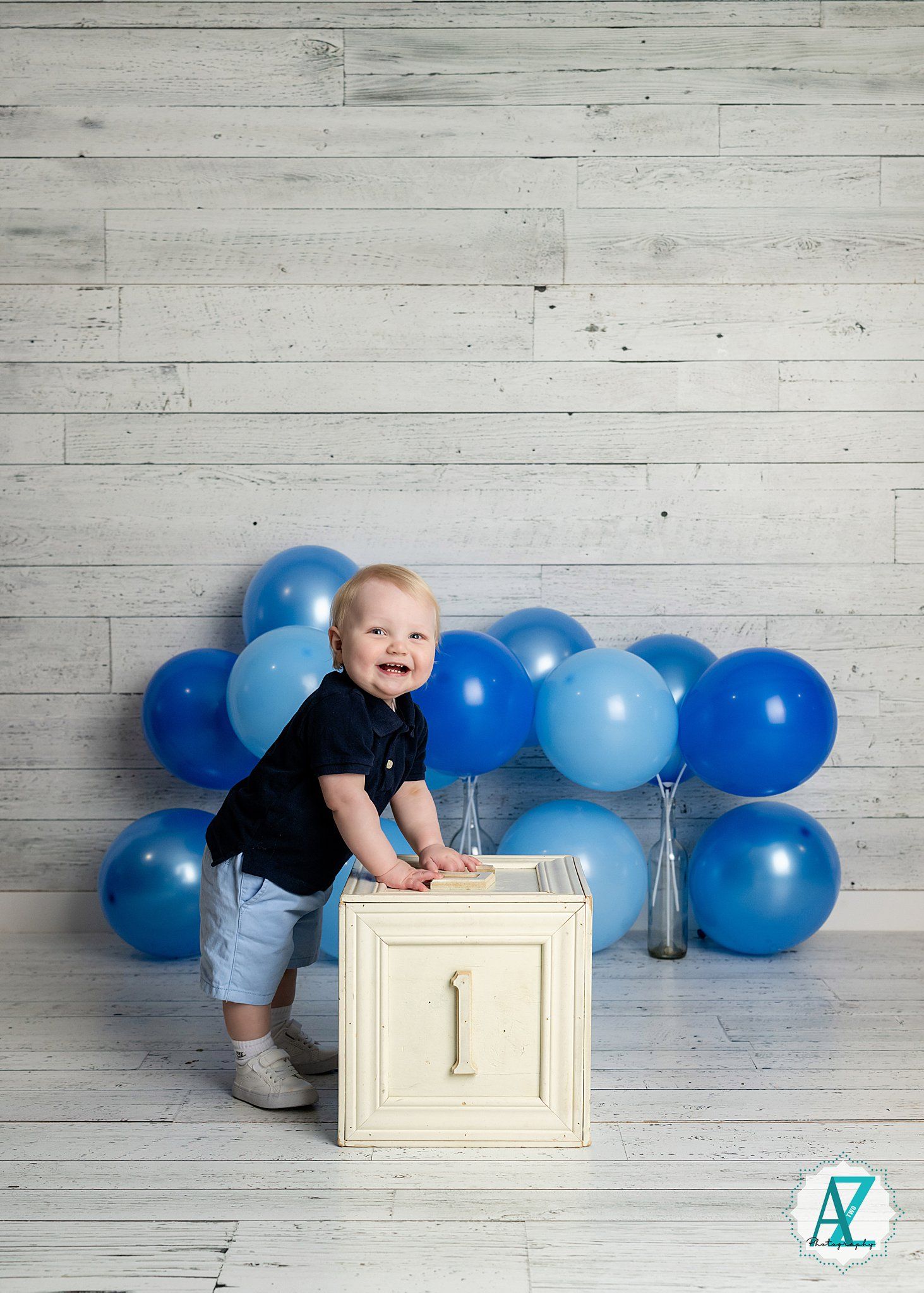 Festive first birthday setup with blue balloons and a white numbered cube against a rustic wood panel backdrop.