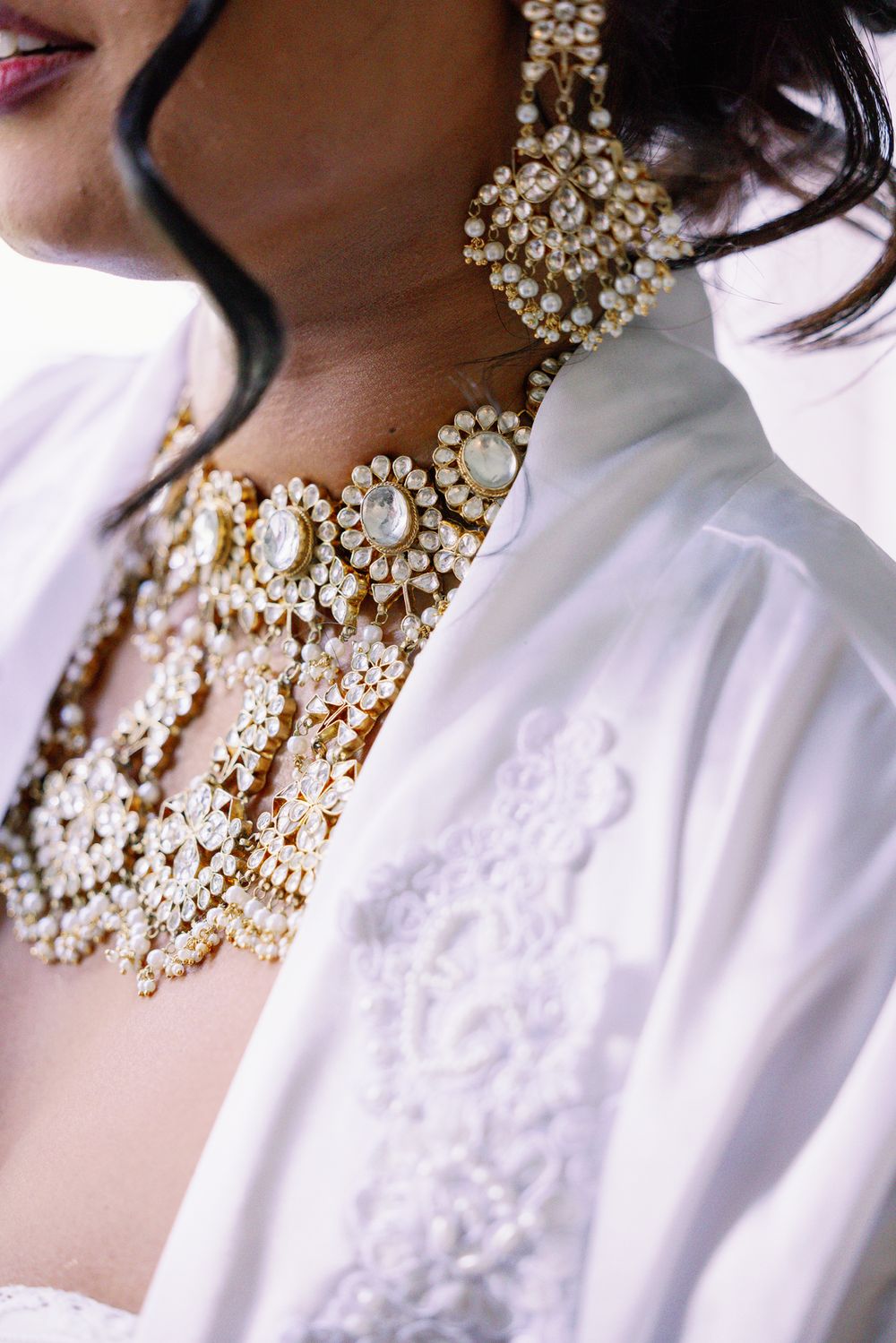 Ornate pearl and crystal bridal jewelry necklace and earrings set against a white lace garment.