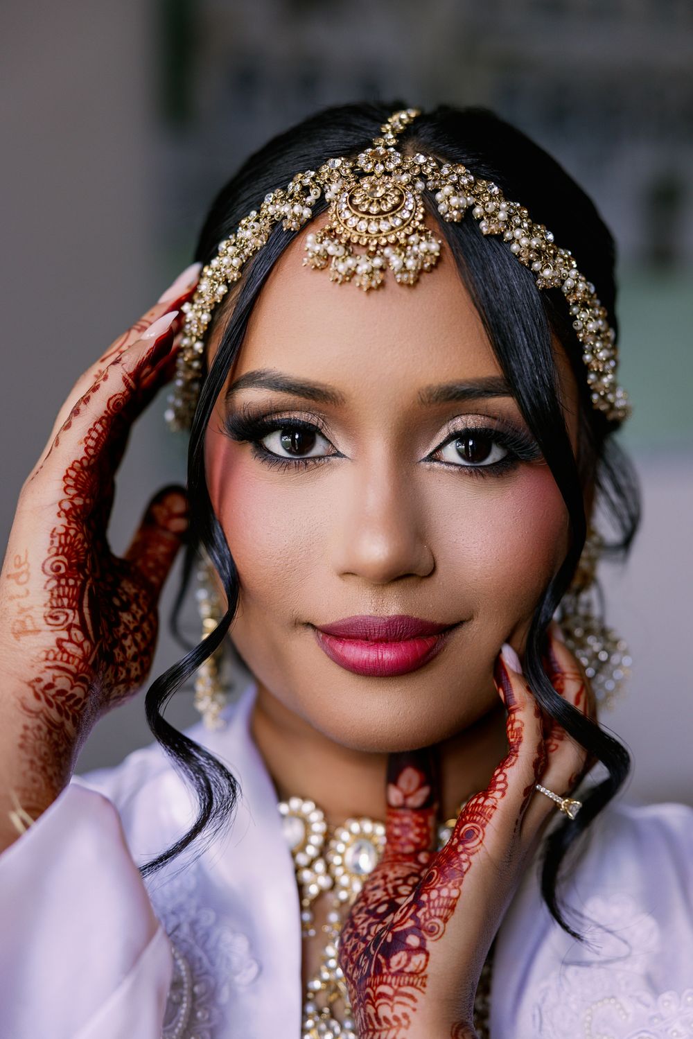 Close-up shot showing bridal jewelry and henna decorated hands framing an ornate headpiece.