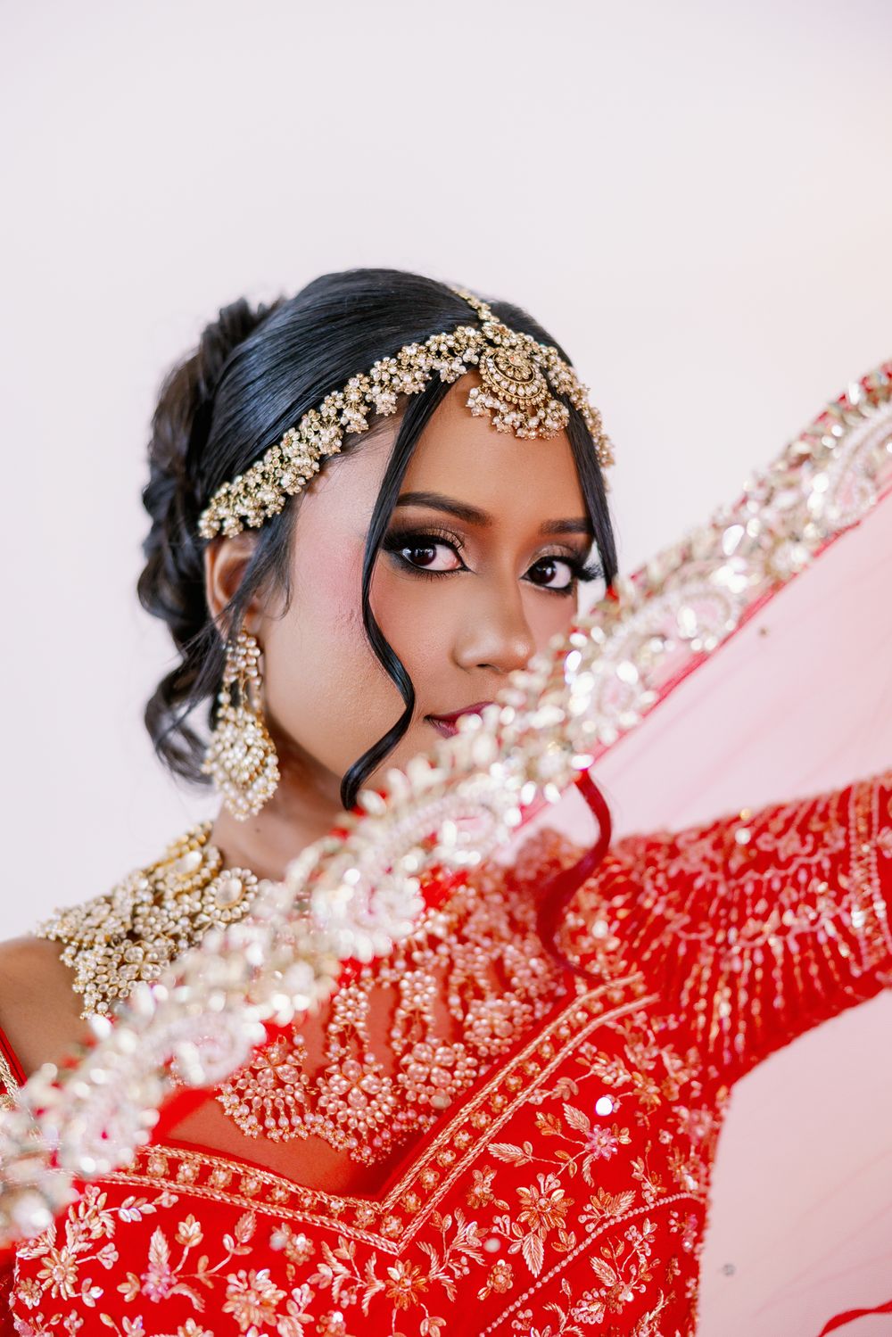 Ornate gold jewelry and traditional red wedding attire create an elegant bridal look against a pink background.