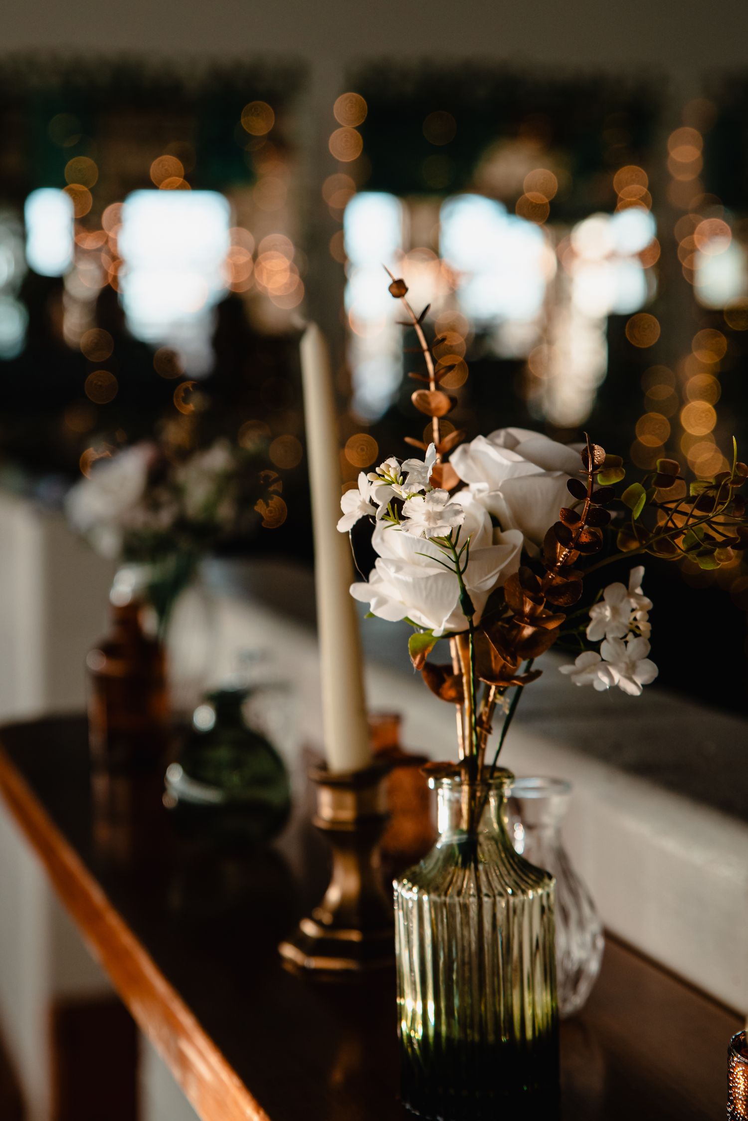 White flowers in a vintage glass vase create an elegant centerpiece with bokeh lights in the dark background.