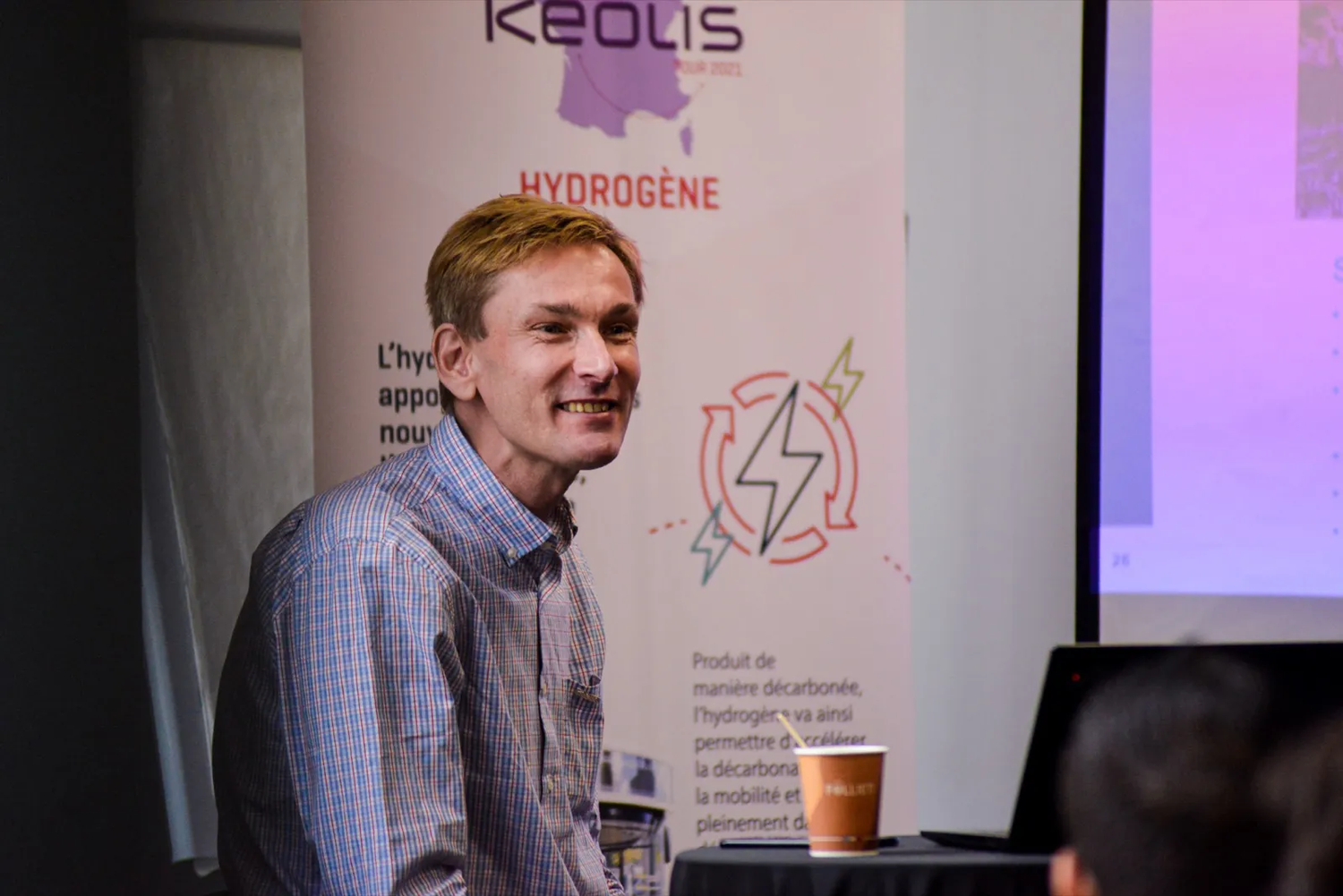 Un intervenant souriant devant un kakémono Keolis Hydrogène, en contexte de présentation ou de salon professionnel.
