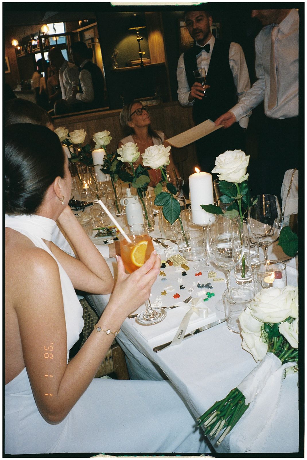 A formal dinner table set with white roses and wine glasses while servers in bow ties attend to guests at an elegant event.