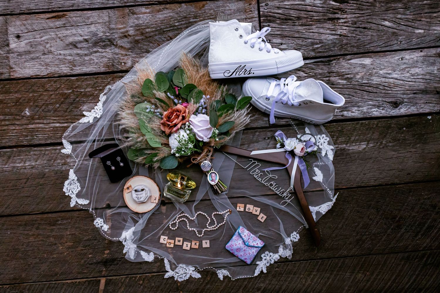 White wedding sneakers and floral decorations arranged on rustic wooden surface.