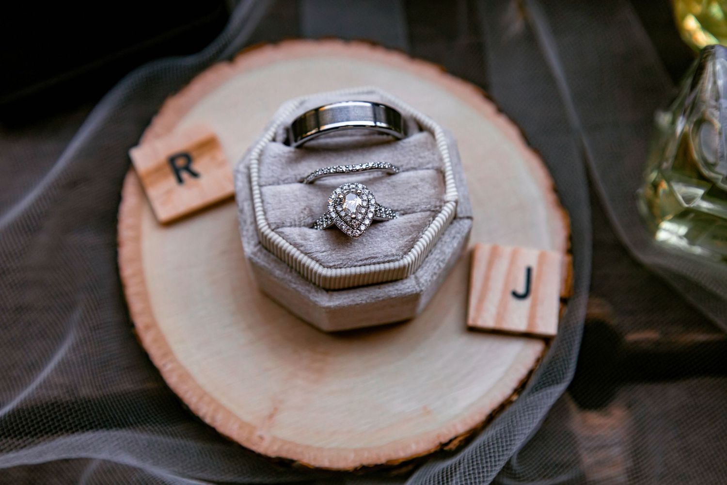 Diamond engagement ring in grey octagonal box displayed on wooden slice.