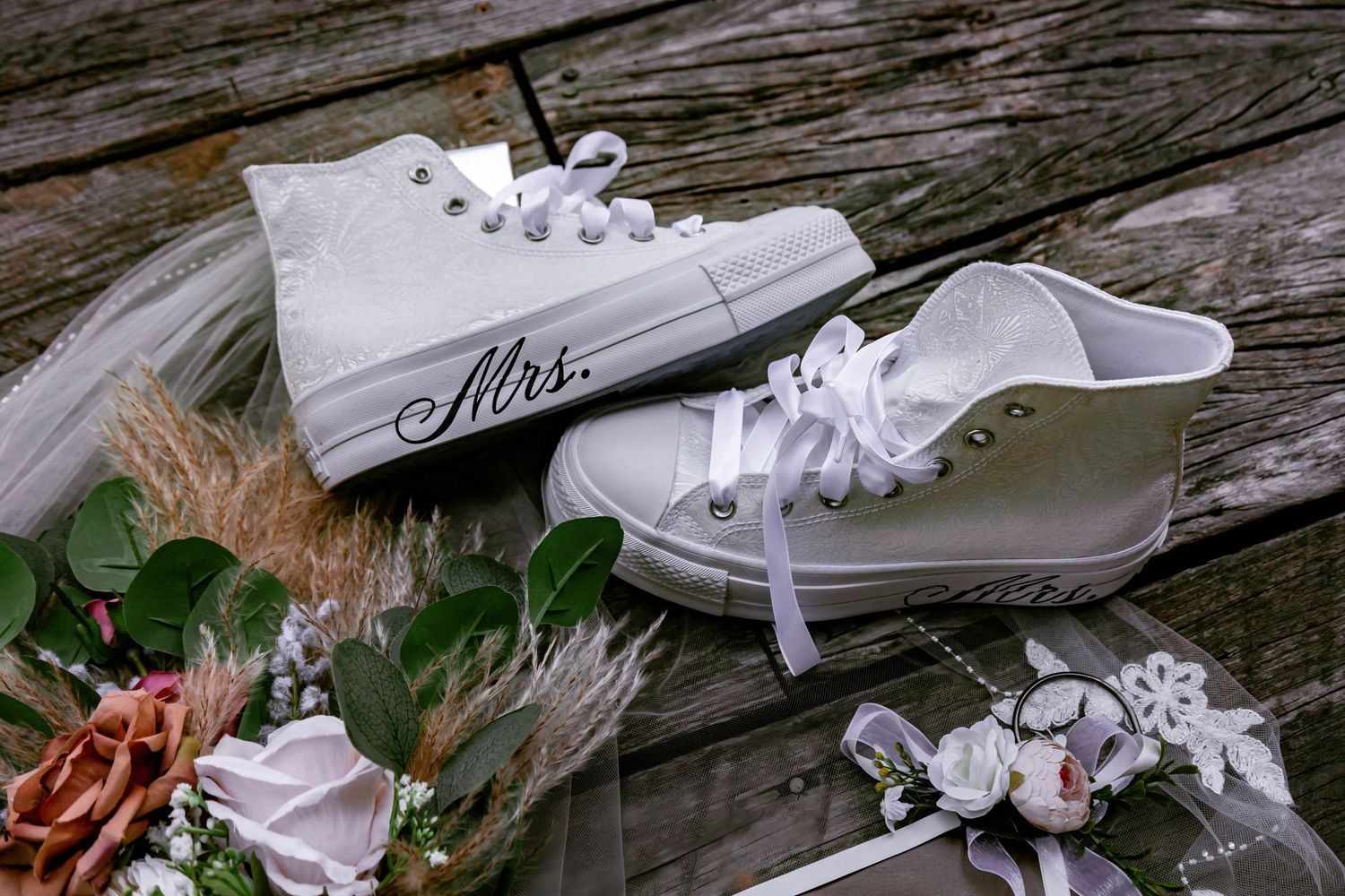 White bridal sneakers with 'Mrs' text decorated with roses on wooden surface.