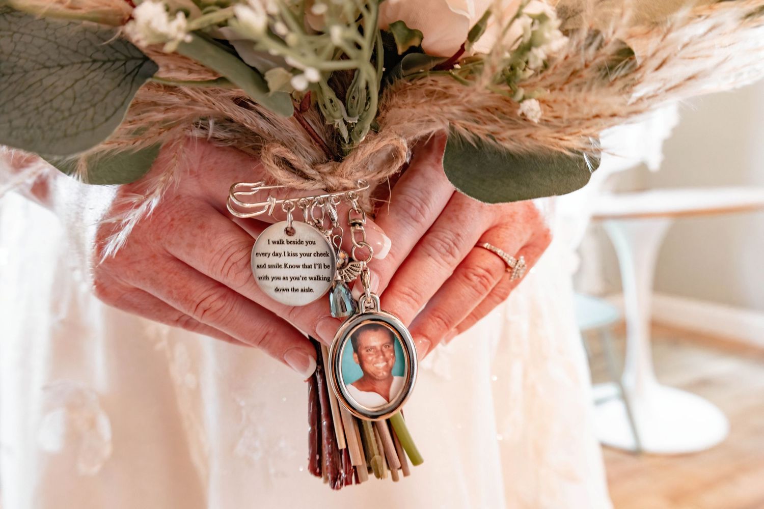 Close-up of hands holding wedding bouquet with sentimental keepsake charm.