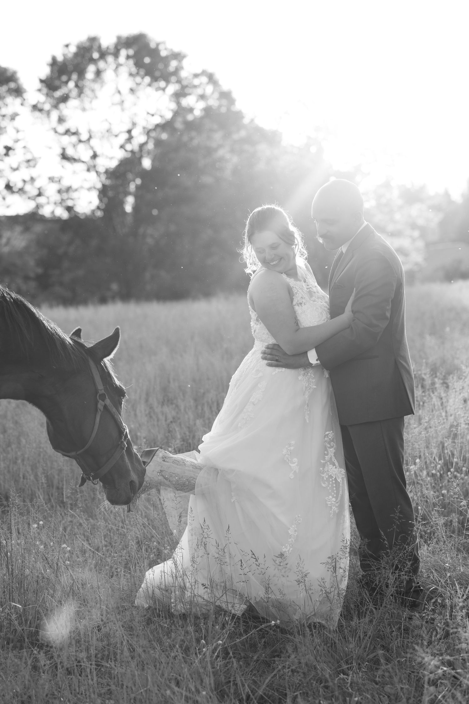 Black and white wedding portraits in a field with a horse at sunset.