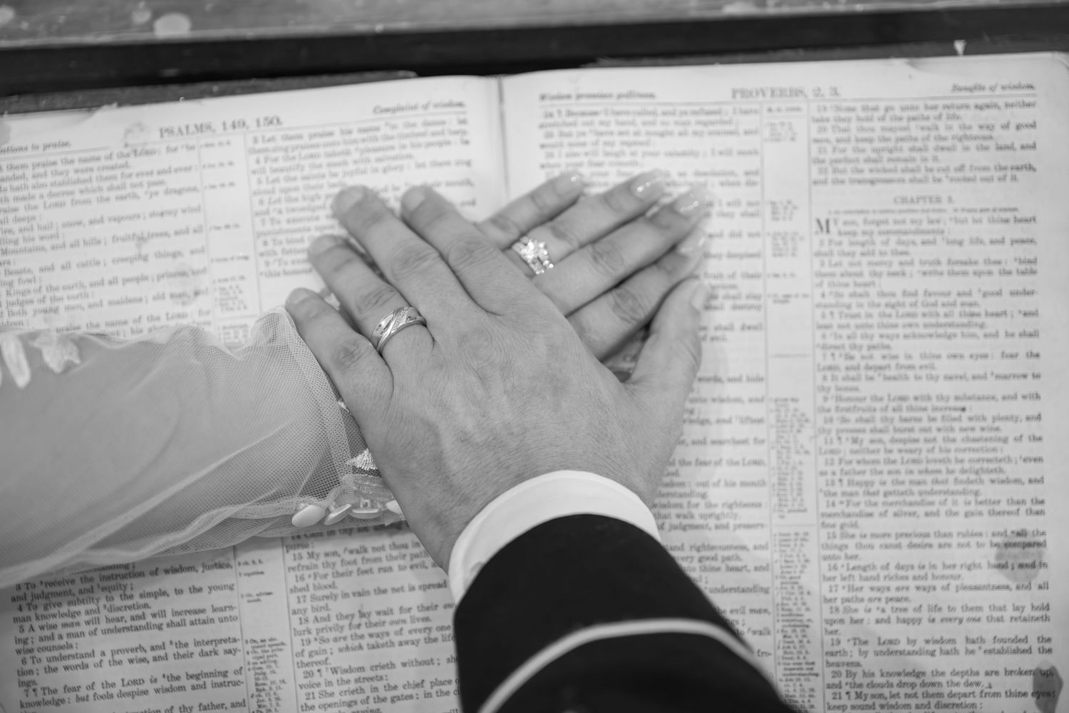Close-up of hands resting on open Bible pages in black and white.