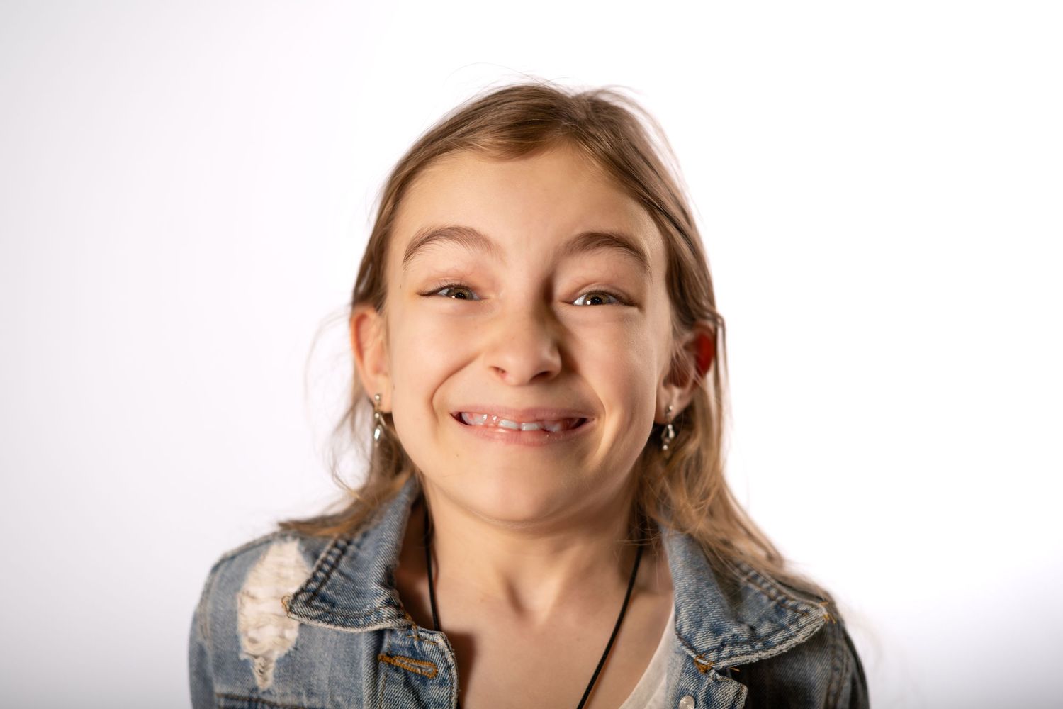 Smiling young girl with braces wearing a denim jacket, portrait photo on white background.